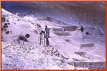 Overview of excavations in progress looking grid north from south end of shelter.  Dave Dibble is at right at plane table. Photo taken by E. Mott Davis in December, 1963, from atop large roof block.