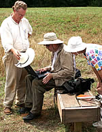 three people looking at a laptop computer outside. One shades the computer screen with a sun hat.