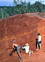 three people excavating an earthen mound