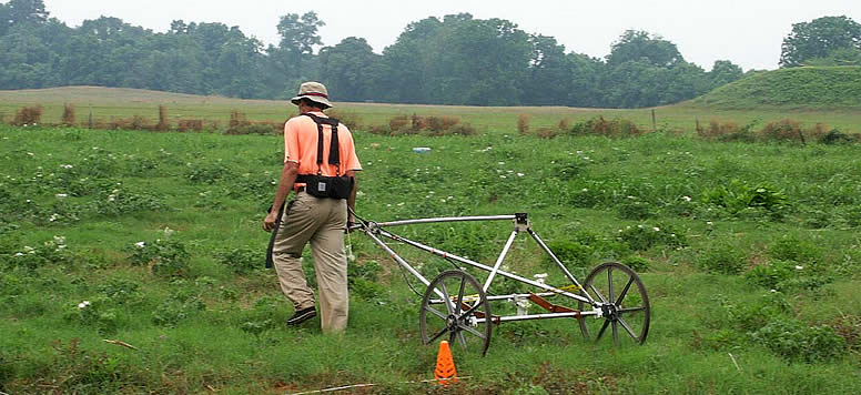 a person pulling a wheeled cart through a green field