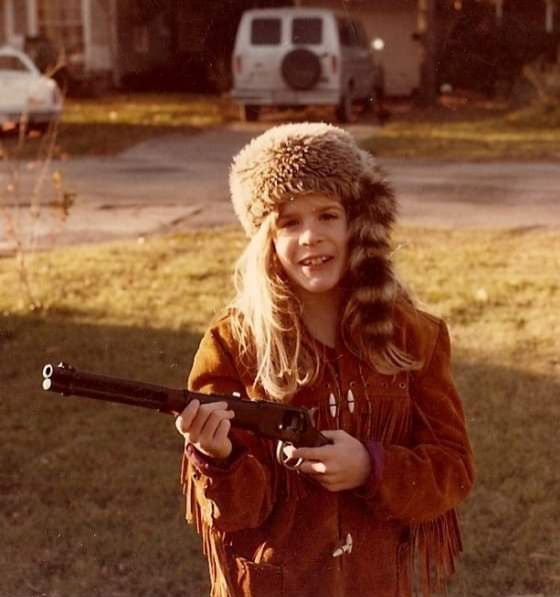 a young girl wearing a raccoon skin cap and leather fringe jacket holding