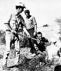 B&W photo of man shoveling dirt into small screen manned by another man and a blond-headed boy.